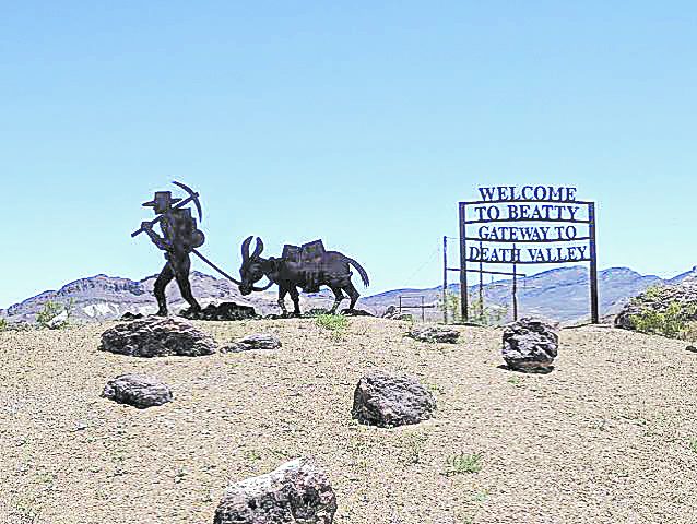 The Welcome to Beatty, Gateway to Death Valley sign beside an iron prospector and burro sculpture on a desert rise